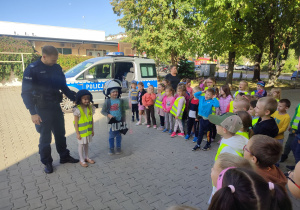 Amelka i Antek ubrani w kaski stoją z Panem Policjantem przed dziećmi.