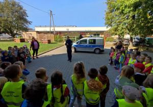 Dzieci stoją przed Panem Policjantem, który opowiada o bezpieczeństwie na drodze.
