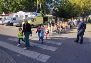 Dzieci z Paniami i Panem Policjanetem przechodzą przez przejście dla pieszych.