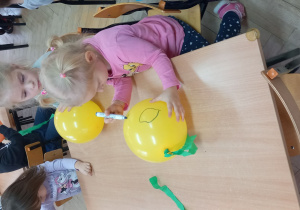 Lenka i Kaja rysują oczy na balonowych dyniach.
