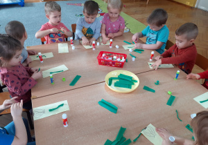 Dzieci przy stole przyklejają „szczypiorek” z bibuły na kartkach z konturem cebuli.