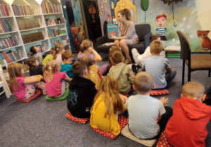 Dzieci siedzą na dywanie i słuchają bajki czytanej przez Panią.