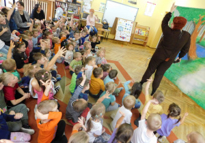 Aktor przebrany za Misia podnosi rękę do góry, dzieci razem z nim podnoszą rączki.