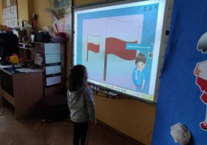 Hania z Maluszków koloruje na tablicy interaktywnej flagę Polski.