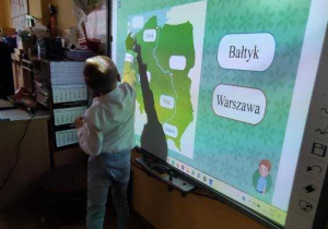 Filip na tablicy interaktywnej odczytuje nazwy miast i regionów Polski.