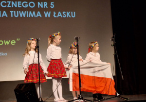 Dziewczynki stoją na scenie i trzymają flagę Polski.