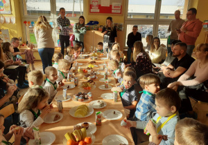 Dzieci w towarzystwie rodziców siedzą za długim stołem.