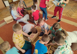 Dzieci na dywanie oglądają karmniki dla ptaków, domki dla owadów i jeży oraz książeczki.