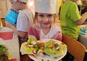 Gabrysia w czapce kucharskiej pokazuje swój talerzyk z kanapkami.