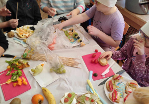 Dzieci siedzą przy stoliku z talerzykami na których są kanapki.