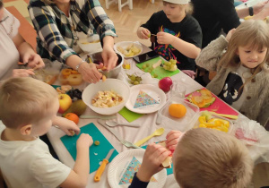 Dzieci z Zosią i jej mamą przy stoliku kroją owoce.