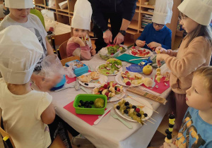 Dzieci przy stoliku przygotowują owocowe przekąski.