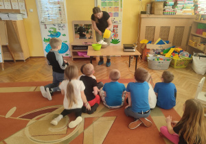 Dzieci siedzą na dywanie, przed nimi mama Olka miesza w misce składniki na gofry.