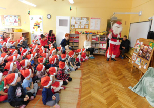 Przedszkolaki witają Mikołaja ciągnącego prezenty.