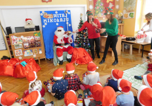 Mikołaj wraz z elfami rozdaje paczki dzieciom.
