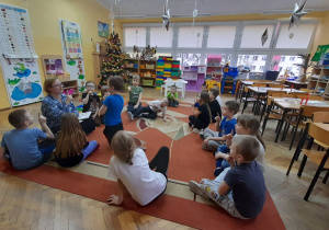 Przedszkolaki siedzą na dywanie i prezentują sposób radzenia sobie ze złością - dmuchanie na „świeczkę” z palca ręki.
