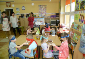 Dzieci biorą udział w knkursie z zawiązanymi oczami na zjadanie pączków