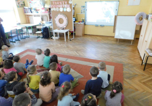 Dzieci siedzą na dywanie oglądają film o pączkach.