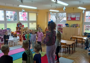 Pani Kamilka wita się z dziećmi piosenką w języku angielskim, a przybyli goście siedzą i obserwują zajęcia.