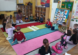 Dzieci siedzą w kole na dywanie podczas zabawy z kartami obrazkowymi.