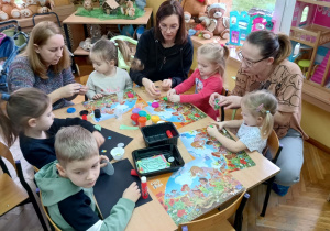 Mamy wraz z dziećmi lepią przy stoliku z masy plastycznej różne kształty.