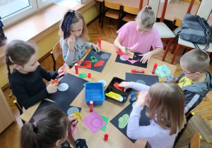 Dzieci siedzą przy stoliku i wykonują pracę plastyczną "Obrazek o kosmosie"