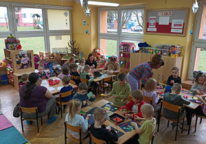 Dzieci z grupy "Słoneczek" wraz z przybyłymi gośćmi siedzą przy stolikach i wykonują prace plastyczne.