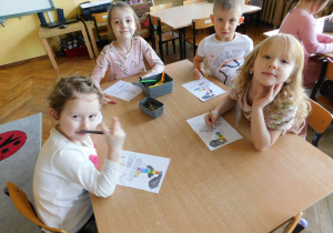 Dzieci siedzą przy stoliku i kolorują malowankę z różnego rodzaju dymami.