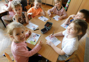 Dzieci kolorują malowankę z różnego rodzaju dymami przy stoliku.