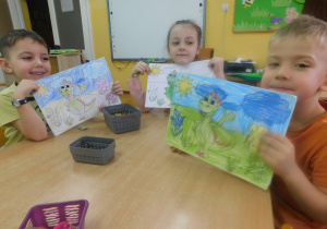 Antoś, Zuzia i Szymon trzymają malowanki Dinka na łące.