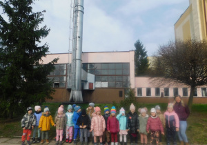 Dzieci z grupy "Biedronek" stoją przy ogromnym kominie z mamą Szymonka.