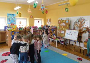 Pani Kamilka pokazuje cyfrę "4", a dzieci szukają jajek w niebieskim kolorze.