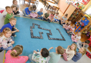 Dzieci z grupy "Biedronek" układają domino na dywanie.