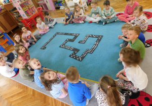 Dzieci z grupy "Biedronek" układają domino na dywanie.