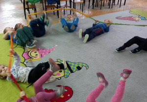 Dzieci trzymając gumę sensoryczną i leżą na dywanie.
