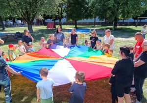 Rodzice i dzieci trzymają chustę animacyjną i przygotowują się do następnego zadania.