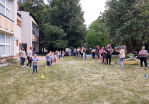 Rodzice przekazują sobie piłkę na pachołku a dzieci na kubeczku.