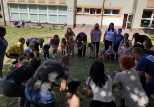 Krasnoludki z rodzicami poruszają gumą sensoryczną ustawieni wokół niej.