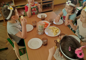 Dzieci przy stoliku jedzą warzywa i owoce.