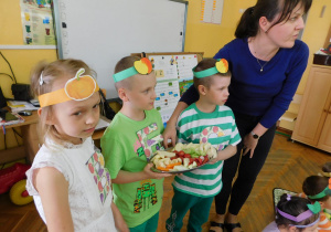 Dzieci trzymają tace z warzywami i owocami.