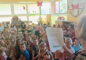 Przedszkolaki uważnie słuchają zasad postępowania z książką, siedząc na dywanie, zwróceni w kierunku pani.