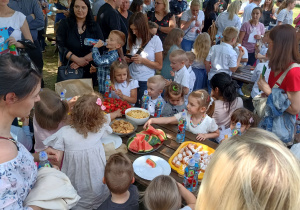 Rodzice i dzieci przy stolikach częstują się owocami i słodkościami.