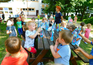 Krasnoludki przy ławce pija wodę.