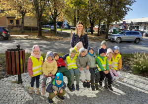 Przedszkolaki siedzą na ławeczce, pozując do zdjęcia z mamą Ali.