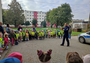 Dzieci stoją z panem policjantem na placu w ogrodzie.