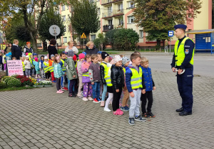 Dzieci z panem Policjantem stoją przed przejściem dla pieszych.