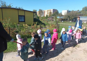 Dzieci spacerują alejkami trzymając się gumy.