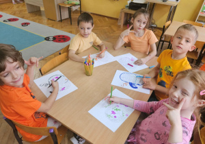 Dzieci przy stoliku kolorują mazakimi malowankę dyni.