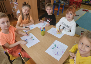 Dzieci przy stoliku kolorują mazakami malowankę dyni.