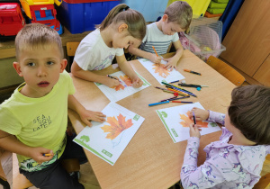 Dzieci tworzą zwierzątko z liścia dorysowując części ciała na kartce.